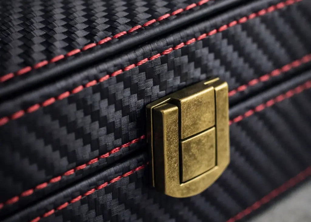 Close-up of a black textured surface  of a faraday box with red stitching and a gold metallic clasp.