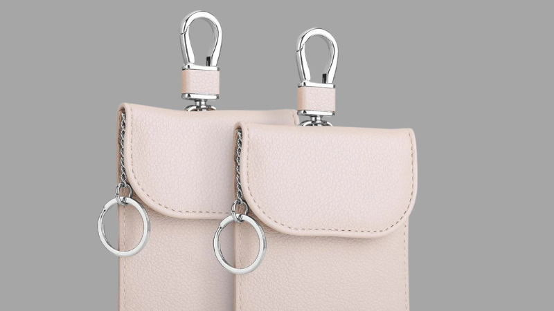 Two beige key faraday pouches with metal hooks on a gray background